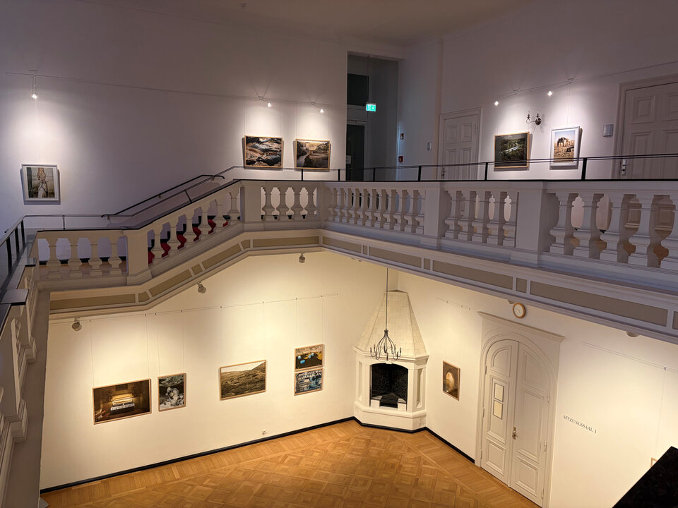 Blick auf eine Galerie mit Kunstwerken an den Wänden und einem offenen Treppenbereich im Vordergrund.