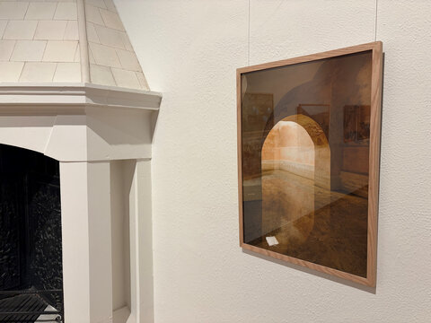 Ein gerahmtes Kunstwerk an einer weißen Wand zeigt einen Raum mit einem Bogen und warmen, erdigen Farben.