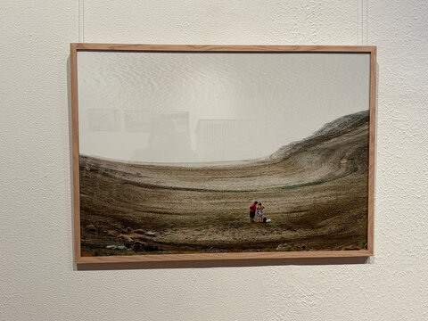 Zwei Personen in einer kargen Landschaft stehen zusammen, umgeben von steiniger Erde und sanften Hügeln im Hintergrund.