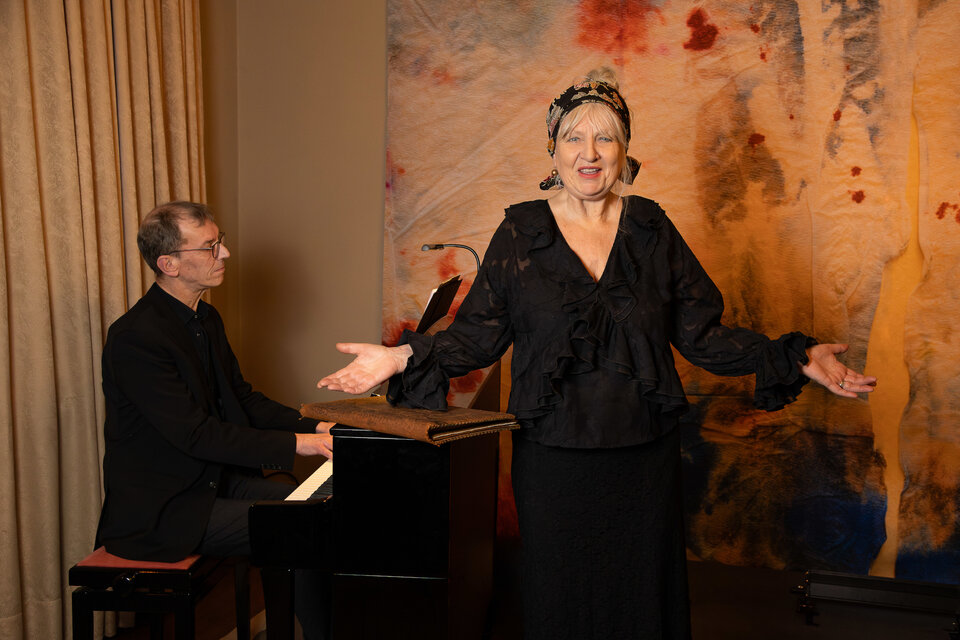 Sängerin in schwarzer Kleidung tritt auf, während ein Pianist am Klavier begleitet. Bunte Wandgestaltung im Hintergrund.