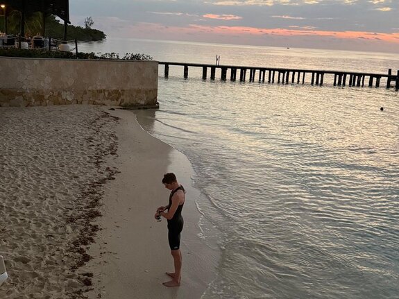 Sportler in einem Neoprenanzug steht am Ufer, blickt auf das Wasser und genießt den Sonnenuntergang.