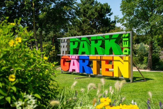 Bunte Buchstaben bilden den Schriftzug "#PARK der GARTEN" vor einer grünen Kulisse mit Blumen.