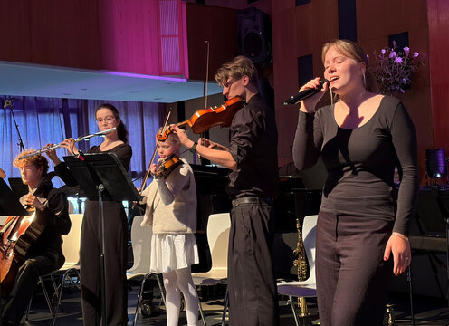 Junge Musikerinnen und Musiker stehen auf einer Bühne, spielen Instrumente und singen während eines Konzerts.