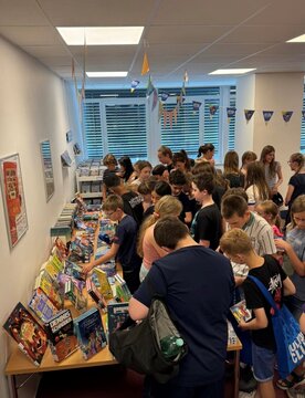 Eine Gruppe von Kindern und Jugendlichen blättert in Büchern und wird von bunten Bannern umgeben.