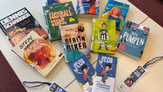 Auf einem Tisch liegen mehrere Bücher und Lesezeichen in bunten Designs. Die Titel sind gut sichtbar, darunter „Fussball Stars“ und „Lilly links laufen“.