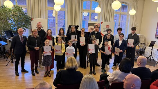 Die Teilnehmer von Jugend musiziert stehen als Gruppe vor dem Publikum. Alle halten eine Urkunde in der Hand.