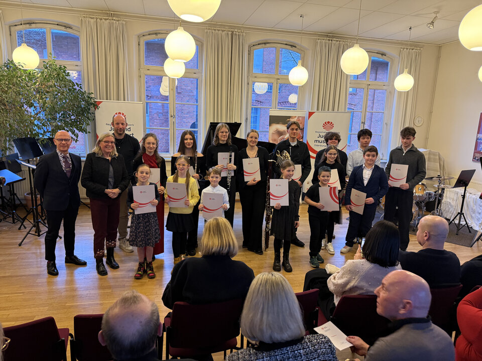 Die Teilnehmer von Jugend musiziert stehen als Gruppe vor dem Publikum. Alle halten eine Urkunde in der Hand.