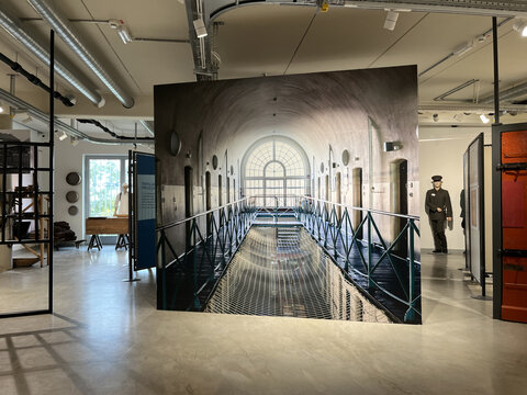 Innenansicht eines Raums mit großen Fenstern und einem langen, handlaufgesicherten Gang. Ausstellungselemente sichtbar.
