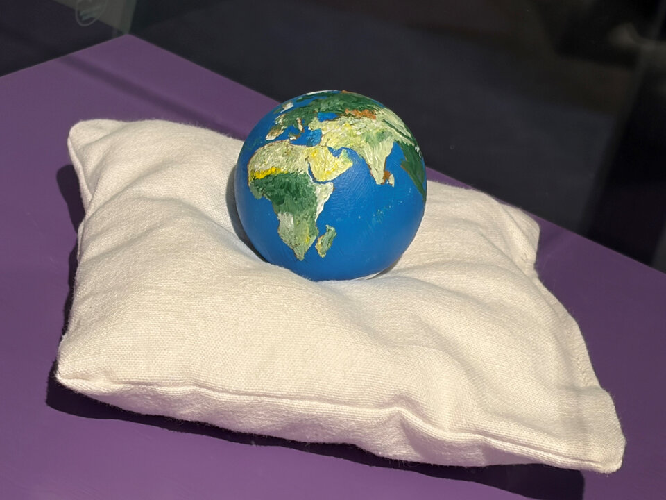 Eine bemalte Erdkugel liegt auf einem weißen Kissen auf einem lila Tisch.