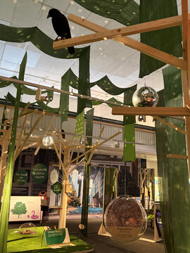 Ein Rabe sitzt auf einem Holzgestell in einem Raum mit grünen Elementen, glitzernden Discoscheiben und interaktiven Ausstellungen.