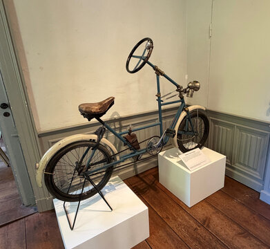 Antikes Fahrrad mit großem Lenkrad in einem Museum, auf einer weißen Säule ausgestellt.