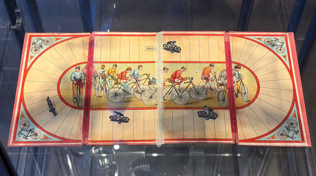Illustration einer Radrennbahn mit spielenden Figuren auf Fahrrädern in lebhaften Farben.