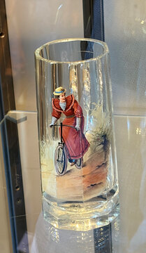 Filigraner Glaskörper mit einer abgebildeten Frau in rotem Kleid auf einem Fahrrad vor einer Landschaft.