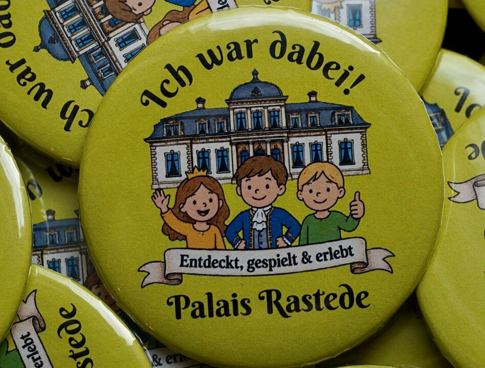 Bunte Ansteckknöpfe mit der Aufschrift „Ich war dabei! Palais Rastede“ und einer Illustration von drei Kindern.