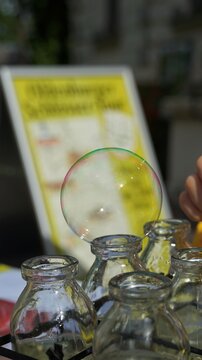 Eine Seifenblase schwebt über einer Reihe von Glasfläschchen, im Hintergrund eine beschriftete Tafel.