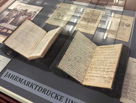 Historische Bücher und Drucke in einer Vitrine, darunter handgeschriebene Seiten und gedruckte Dokumente.