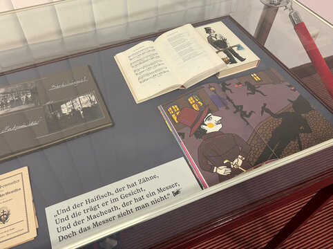 Ein Ausstellungsvitrinen-Inhalt mit einem offenen Buch, Illustrationen und einer Texttafel.