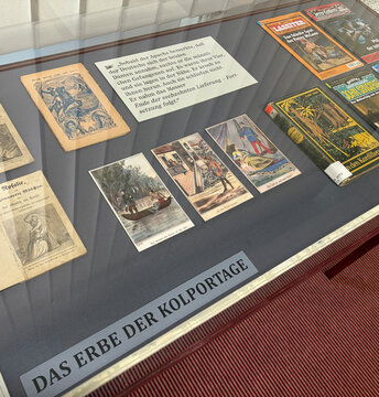 Vitrine mit historischen Dokumenten und Illustrationen zum Thema Kolportage, beschriftet „DAS ERBE DER KOLPORTAGE“.