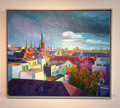 Blick auf eine städtische Landschaft mit bunten Dächern und Türmen, unter einem dramatischen Himmel.