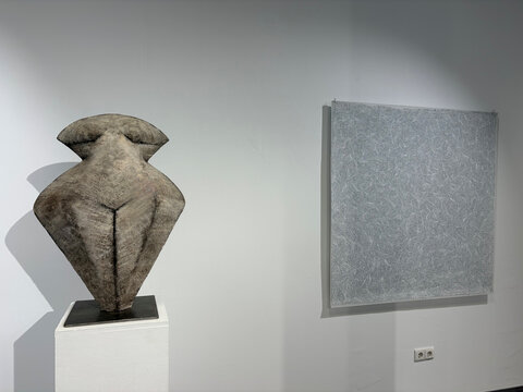 Abstrakte Skulptur in Form einer weiblichen Figur neben einem gleichfarbigen, strukturierten Bild an der Wand.