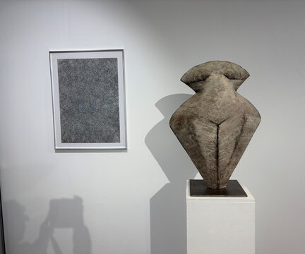 Skulptur einer weiblichen Figur aus Stein neben einem rechteckigen gerahmten Kunstwerk an einer weißen Wand.