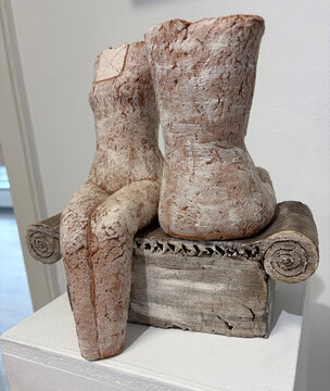 Eine Skulptur mit zwei sitzenden Figuren auf einem Sockel, aus leicht rissiger, grauer und roter Keramik.