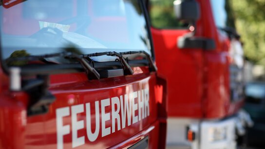 Rotes Feuerwehrfahrzeug im Vordergrund mit gut sichtbarem Schriftzug „FEUERWEHR“ und einem weiteren Fahrzeug im Hintergrund.