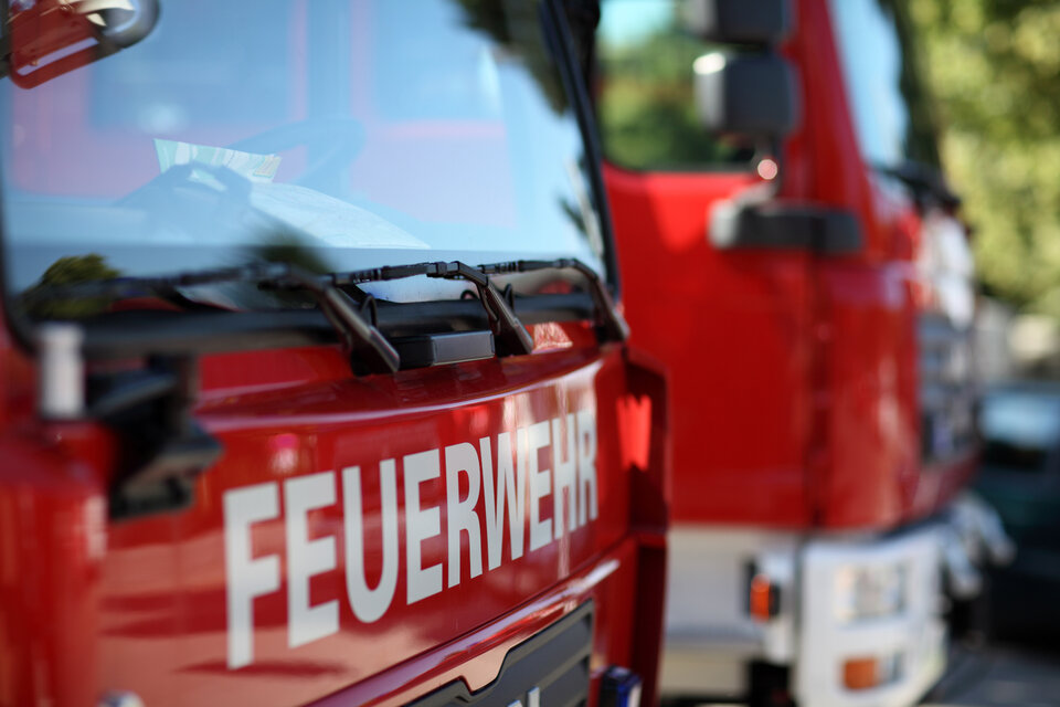 Rotes Feuerwehrfahrzeug im Vordergrund mit gut sichtbarem Schriftzug „FEUERWEHR“ und einem weiteren Fahrzeug im Hintergrund.