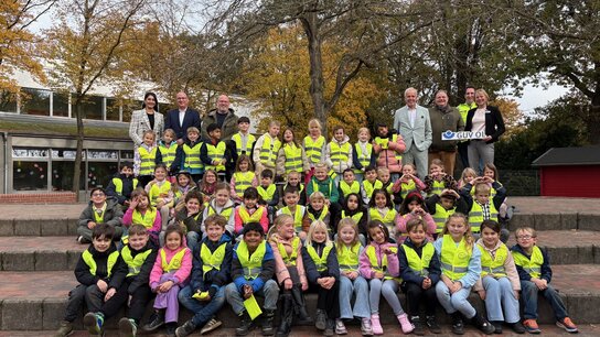 Gruppe von Schülern in leuchtenden Westen, stehen auf einer Treppe, umgeben von Erwachsenen, in herbstlicher Umgebung.