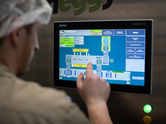 Mitarbeiter bedient ein Touchscreen-Display mit einer grafischen Benutzeroberfläche zur Maschinensteuerung.