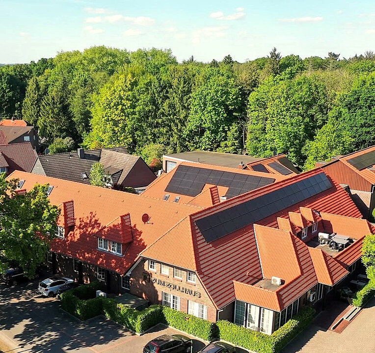 Dächer mit roten Ziegeln und grüner Baumlandschaft im Hintergrund, mehrere Gebäude, darunter das Gasthaus Zum Zollhaus.