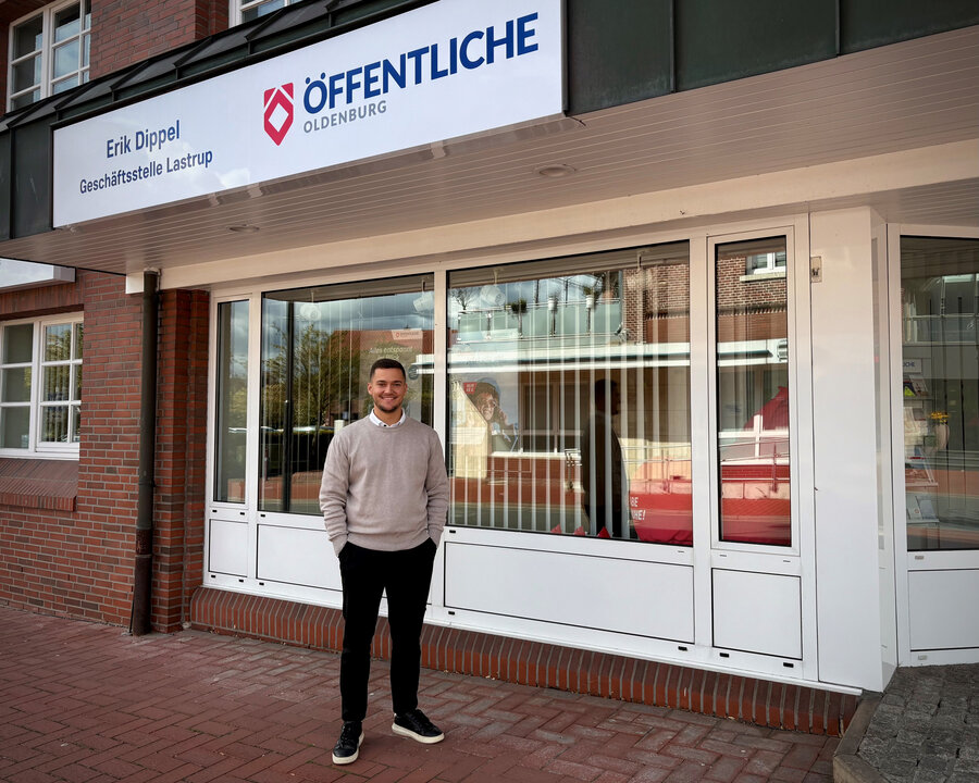 Mann steht vor der Geschäftsstelle "ÖFFENTLICHE" in Oldenburg, mit einem Schild und großen Fenstern im Hintergrund.