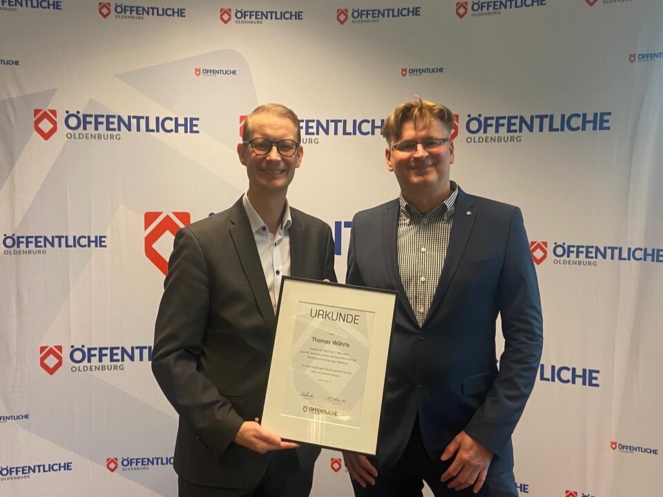 Frank Schwerter und Thomas Wöhrle stehen vor einem Banner mit dem Schriftzug "ÖFFENTLICHE OLDENBURG" und halten eine Urkunde in der Hand.
