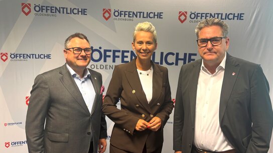 Ralf Kunze, Silvia Breher und Jürgen Müllender stehen vor einer Werbebande mit Logos der Öffentliche Oldenburg