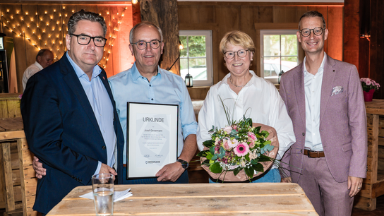 Jürgen Müllender, Josef Oevermann, Sigrid Oevermann und Frank Schwerter stehen an einem Tisch in einer Partyscheune. Josef Overmann hat eine Urkunde in der Hand.