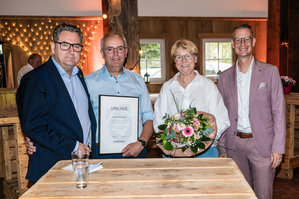 Jürgen Müllender, Josef Oevermann, Sigrid Oevermann und Frank Schwerter stehen an einem Tisch in einer Partyscheune. Josef Overmann hat eine Urkunde in der Hand.