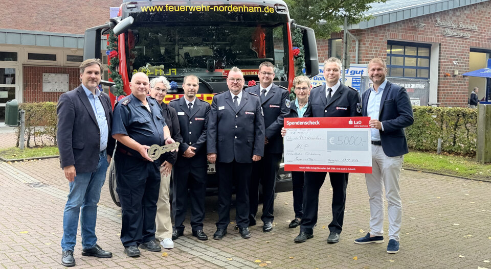 Gruppierung von Feuerwehrmitgliedern und Unterstützern vor einem Feuerwehrfahrzeug, das einen Scheck über 3.000 Euro präsentiert.