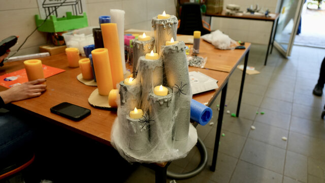 Dekorative Kerzen in verschiedenen Höhen auf einem Tisch, umgeben von weiteren farbigen Kerzen und Bastelmaterialien.