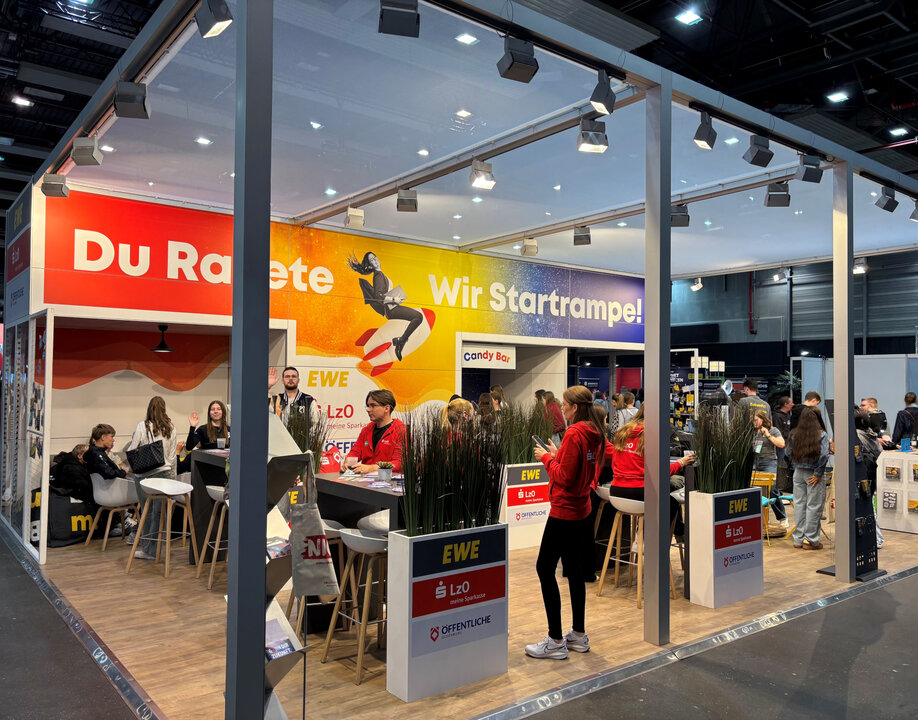 Messestand mit mehreren Personen, Stehtischen und Bannern, die "Du Rakete" und "Wir Startrampe!" zeigen.