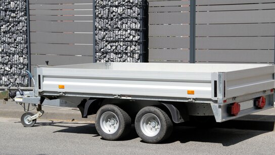 EIn Anhänger ohne Dach steht vor einem Gartenzaun.