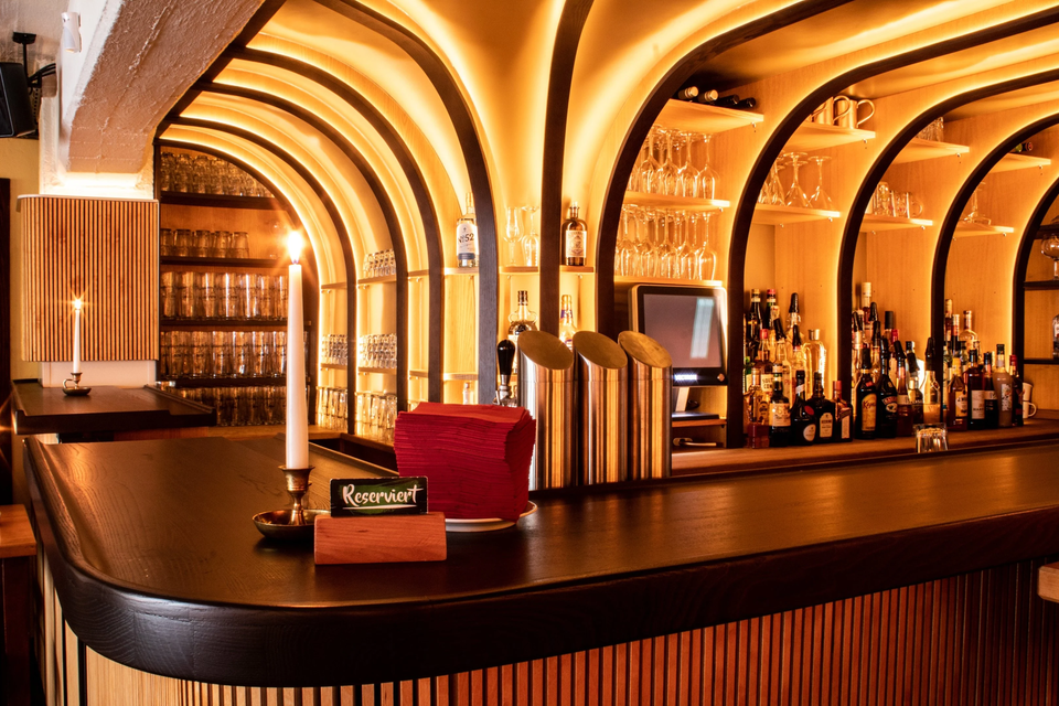 Ansicht eines Bartresen. Vorne eine Reserviert-Schild und eine brennende Kerze. Im HIntergrund die Bar mit Getränken und Gläsern.